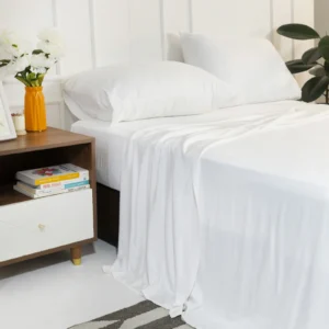 Cama vestida con sábanas de viscosa de bambú color blanco junto a una mesa de noche con flores