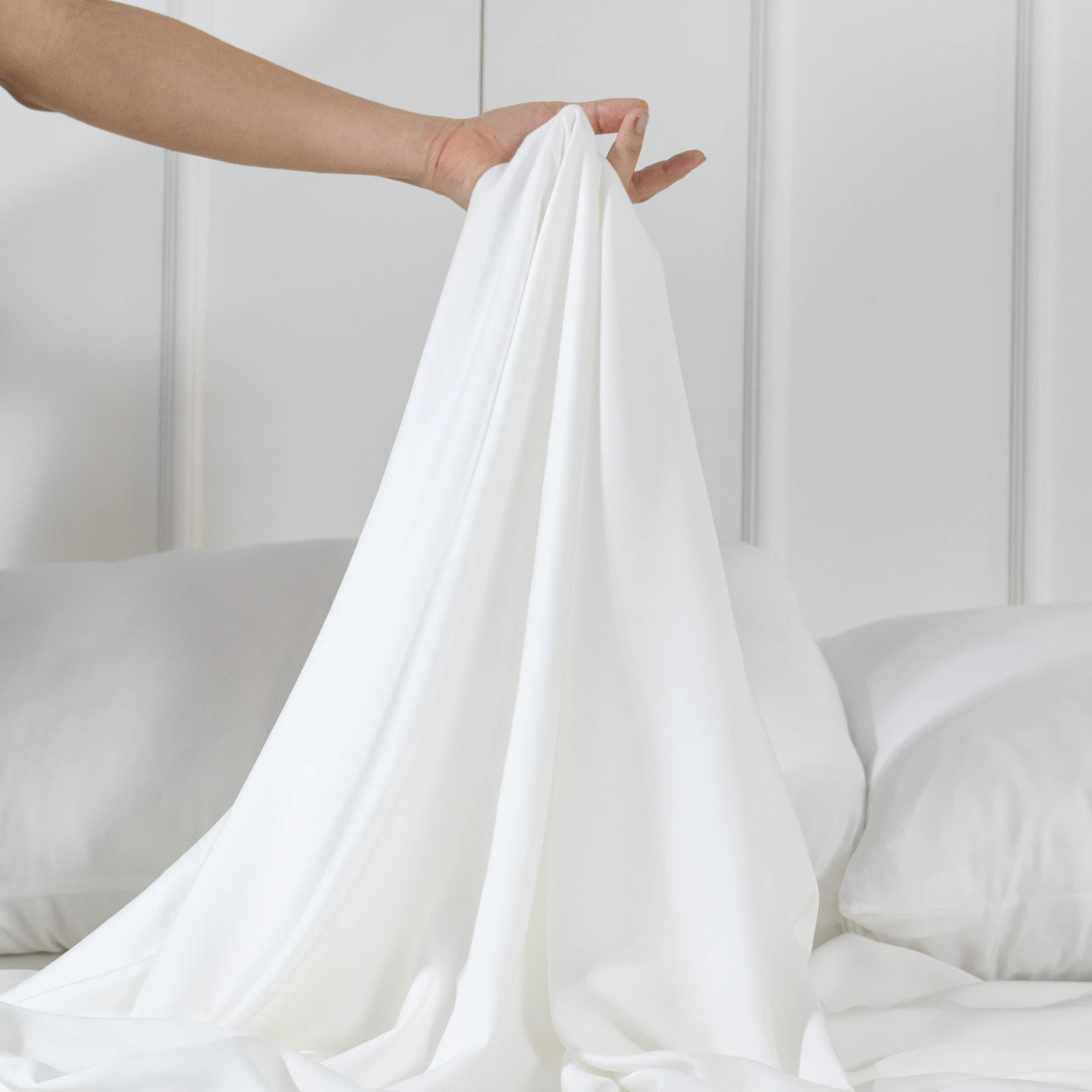 Sábana de viscosa de bambú color blanco levantada con la mano para mostrar su caída