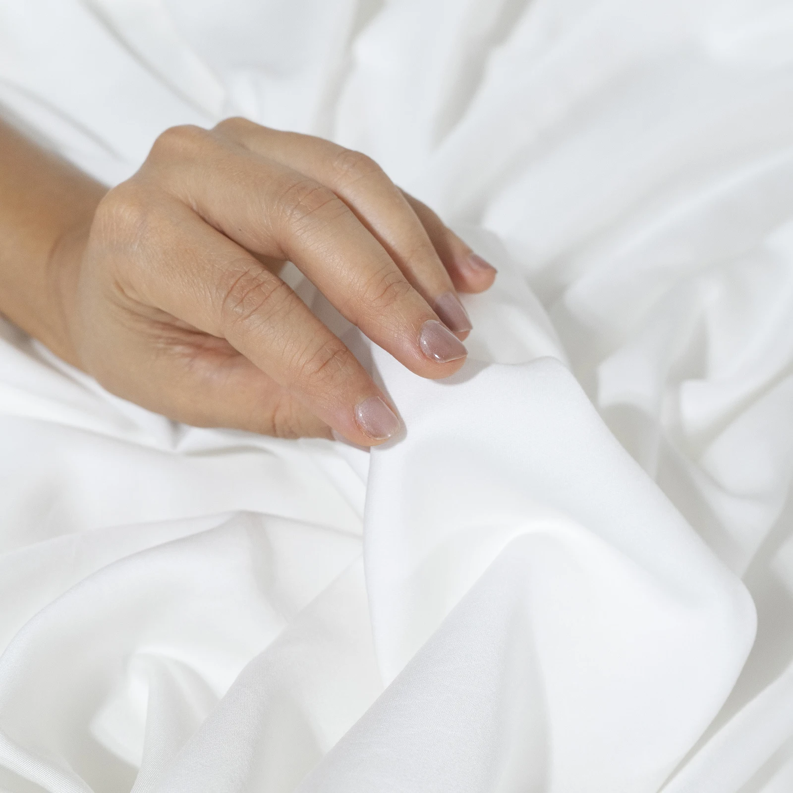 Mano apoyada sobre la sábana de viscosa de bambú color blanco mostrando la suavidad del tejido